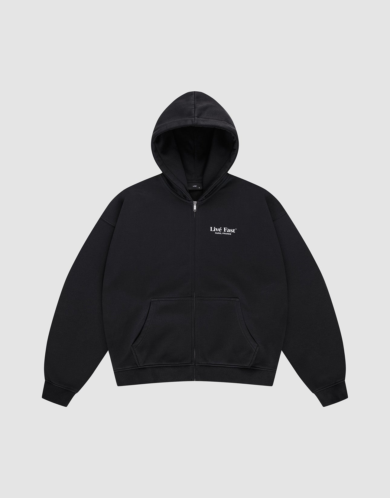 The LFDY Paris Hooded Zip by LIVE FAST DIE YOUNG is a black oversized zip-up hoodie with front pockets, a hood, and small white "Live Fast" text on the left chest, made from soft Baumwolle and shown on a light gray background.