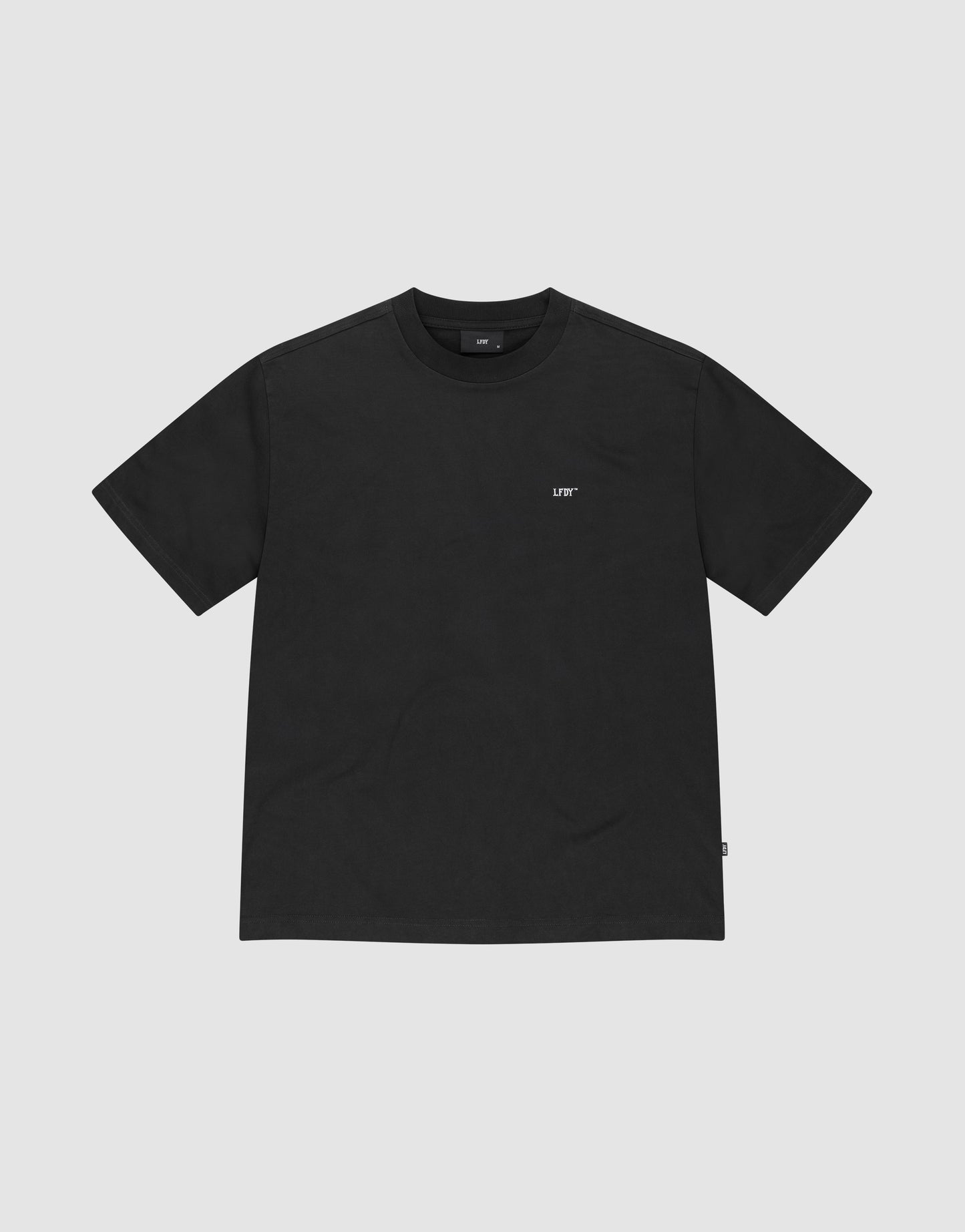 The Basic Trademark Tee by LIVE FAST DIE YOUNG is an Oversize Fit black short-sleeve shirt with a small white LIFE logo on the left chest, made from 100% Baumwolle and shown on a light gray background.