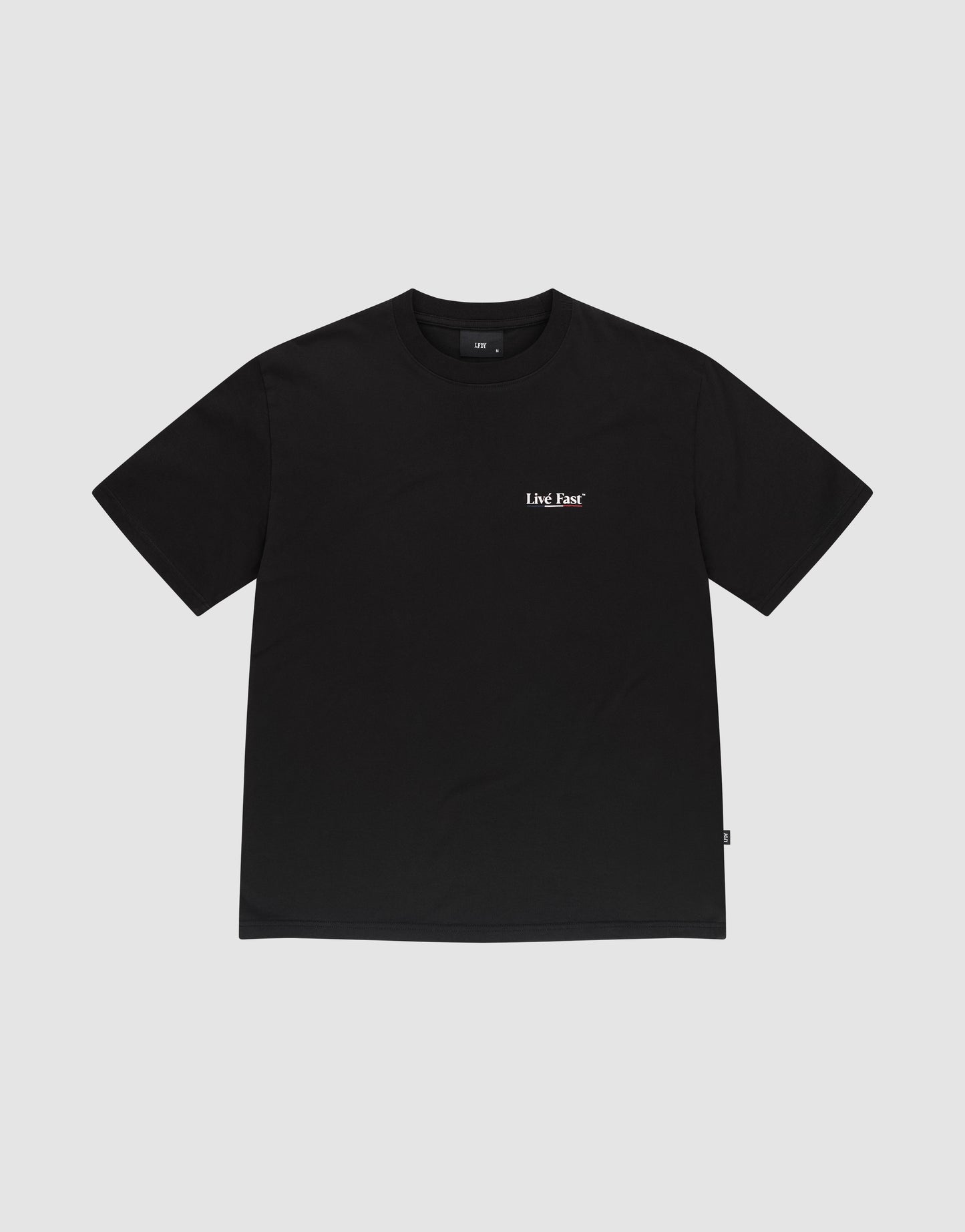The Live Fast Paris Tee by LIVE FAST DIE YOUNG is a plain black Regular Fit short-sleeve t-shirt made from 100% Baumwolle, featuring a small white LMC Bar logo on the left chest, shown on a light gray background.