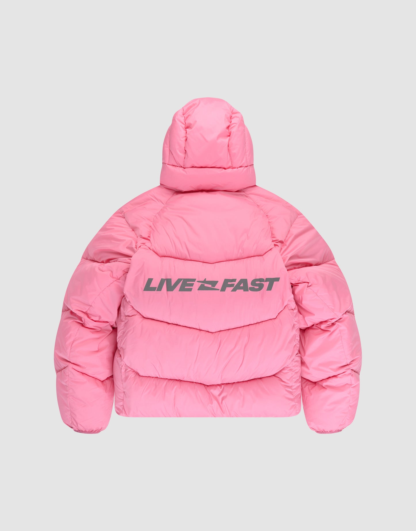 The Live Fast Puffer Jacket by LIVE FAST DIE YOUNG is a pink nylon oversized jacket with a hood, shown from the back, and features a bold reflective "LIVE FAST" print in gray across the upper back.