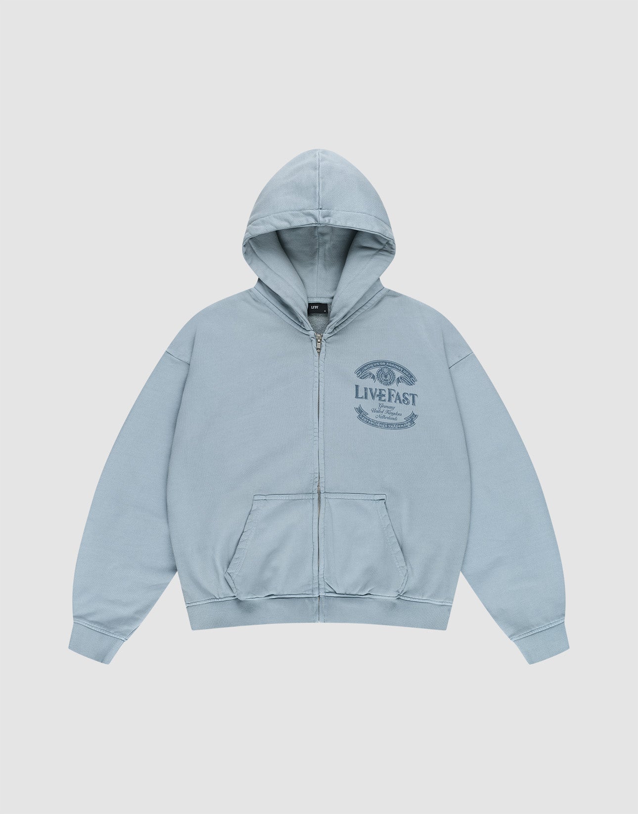The LFDY 55 Hooded Zip by LIVE FAST DIE YOUNG is a light blue, oversized zip-up hoodie with a front pocket, hood, and dark blue LIVE FAST graphic with laurel wreath on the left chest. Made from 100% Baumwolle. Shown laid flat on a white background.