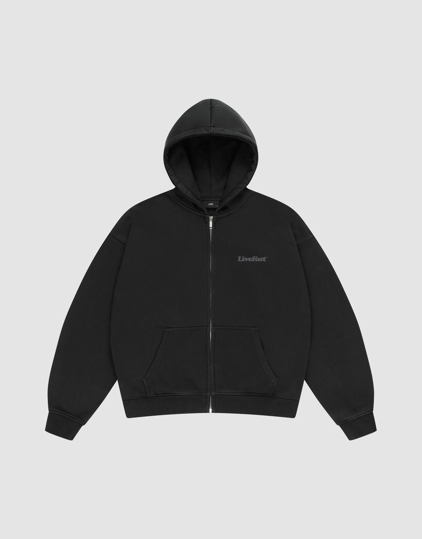 The BASIC 510 HOODED ZIP by LIVE FAST DIE YOUNG is an oversize fit black zip-up hoodie with a hood and front pockets, shown on a light gray background. “LiveFast” is subtly printed on the left chest.