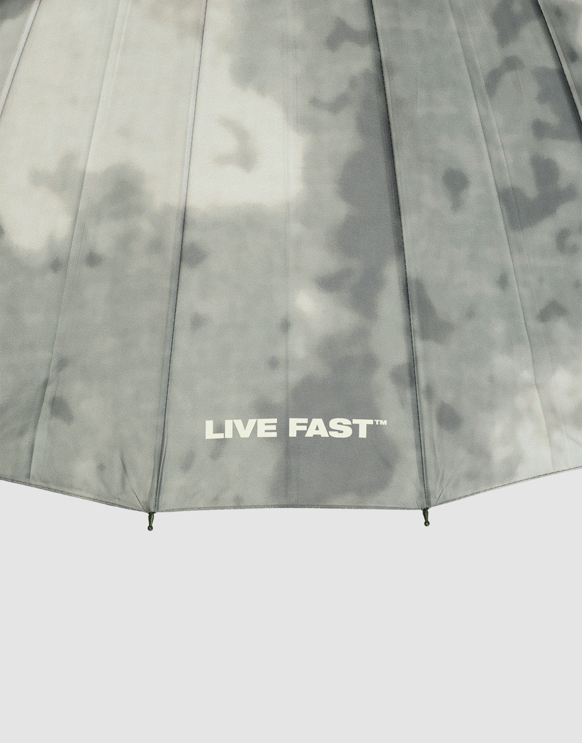 A close-up of the LFDY Umbrella by LIVE FAST DIE YOUNG, featuring a grey cloudy pattern, stabile Rahmenkonstruktion, and “LIVE FAST™” printed in white near the bottom edge.