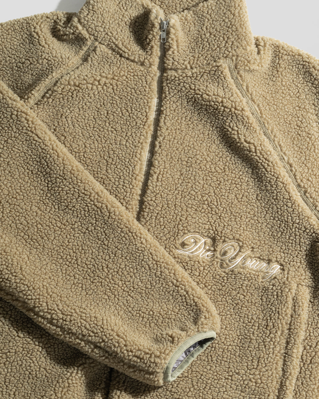 The LFDY Teddy Jacket by LIVE FAST DIE YOUNG is a beige fleece with an oversize fit, high collar, and embroidered "Die Young" text on the left chest. Its soft texture and practical zipper add comfort, shown here against a plain white background.