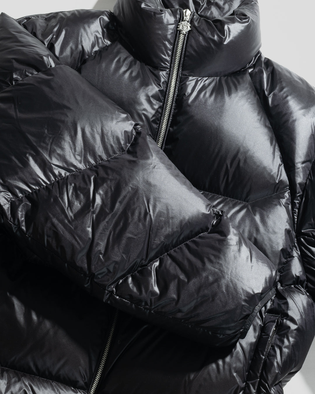 Close-up of the shiny black Live Fast Down Jacket by LIVE FAST DIE YOUNG, featuring a visible front zipper and quilted sections. The glossy, water-repellent fabric reflects light, accentuating its puffy texture and modern style.