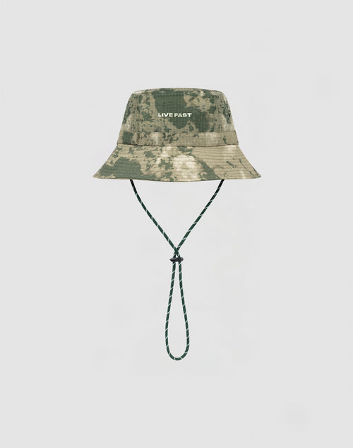 The LIVE FAST DIE YOUNG Camo Nylon Bucket Hat in green camouflage features strapazierfähigem Nylon Stoff, a white silicone LIVE FAST print on the front, and a matching green Kinnband, shown on a plain white background.