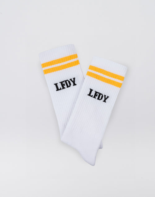 The LFDY Logo Socks (2 Pack) by LIVE FAST DIE YOUNG feature a white ribbed design with two yellow stripes and black LFDY text below. Made from 82% cotton, they’re easy-care—please follow the care instructions.