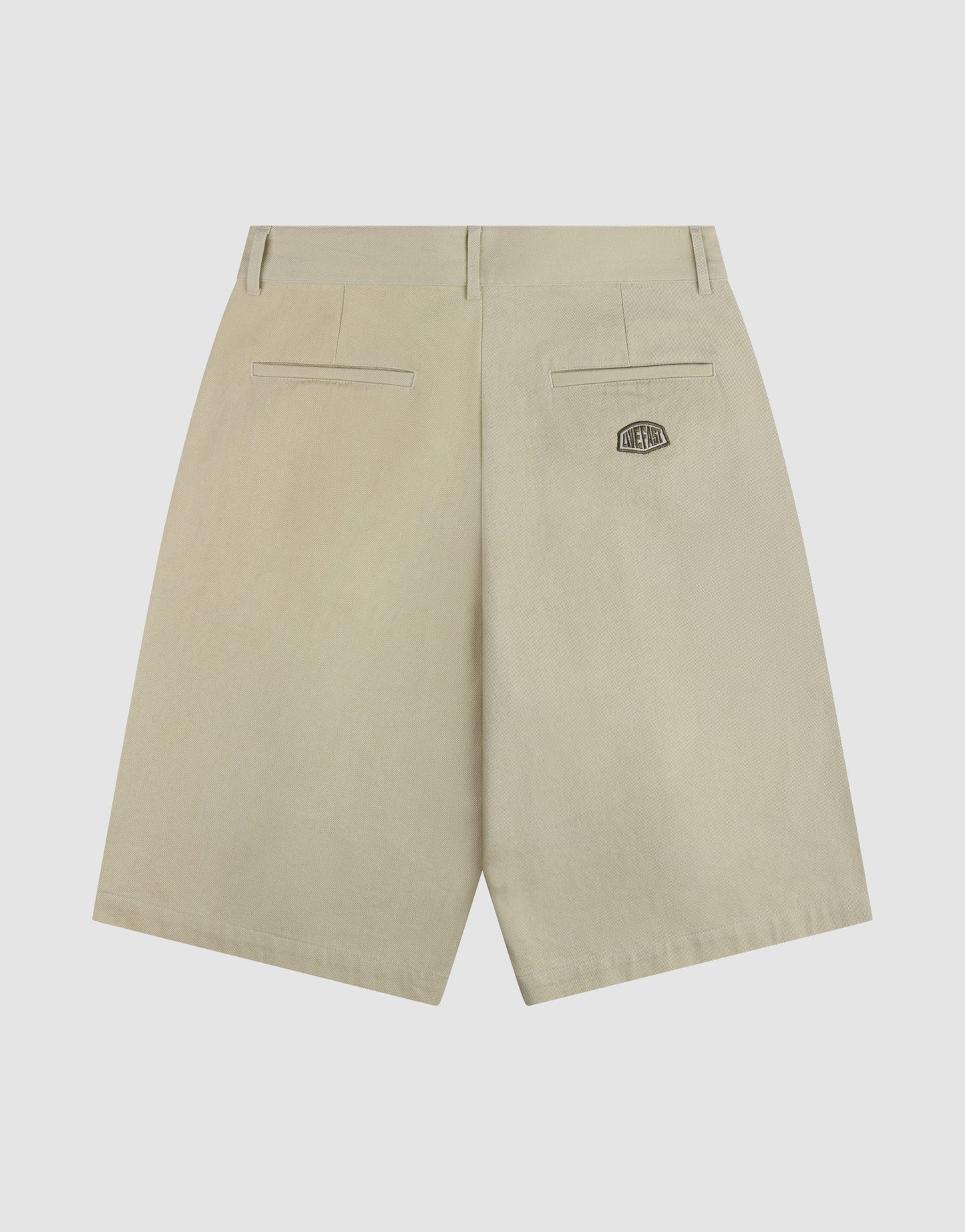 The LFDY Twill Shorts by LIVE FAST DIE YOUNG are beige cotton shorts with an oversize fit, wide straight leg, two back welt pockets, and a small black patch with white text above the right pocket for a relaxed look.