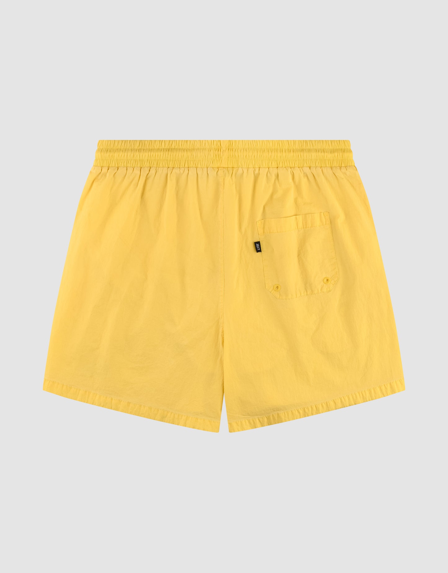 The Live Fast Swim Shorts by LIVE FAST DIE YOUNG feature an elastikbund and single back pocket in a tinted yellow wash, shown flat on a light gray background with the back side of the regular fit garment displayed.