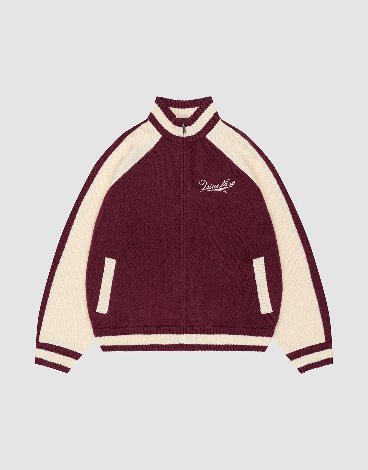 The Boxy Knit Zip Jacket by LIVE FAST DIE YOUNG features a maroon body, cream sleeves, collar and cuff stripes, two cream front pockets, and a white embroidered Logo-Strick script on the left chest. Background is light gray.