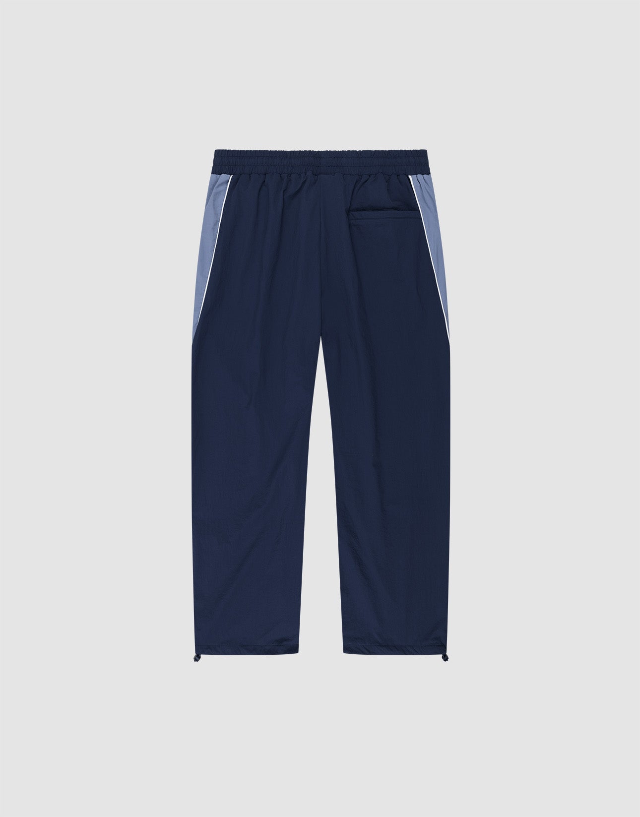 The LIVE FAST DIE YOUNG Basic Nylon Trackpants in navy feature light blue side panels, an Elasticbund waistband, a back pocket, and adjustable drawstring hems. Relaxed Wide Fit silhouette shown against a plain light background.
