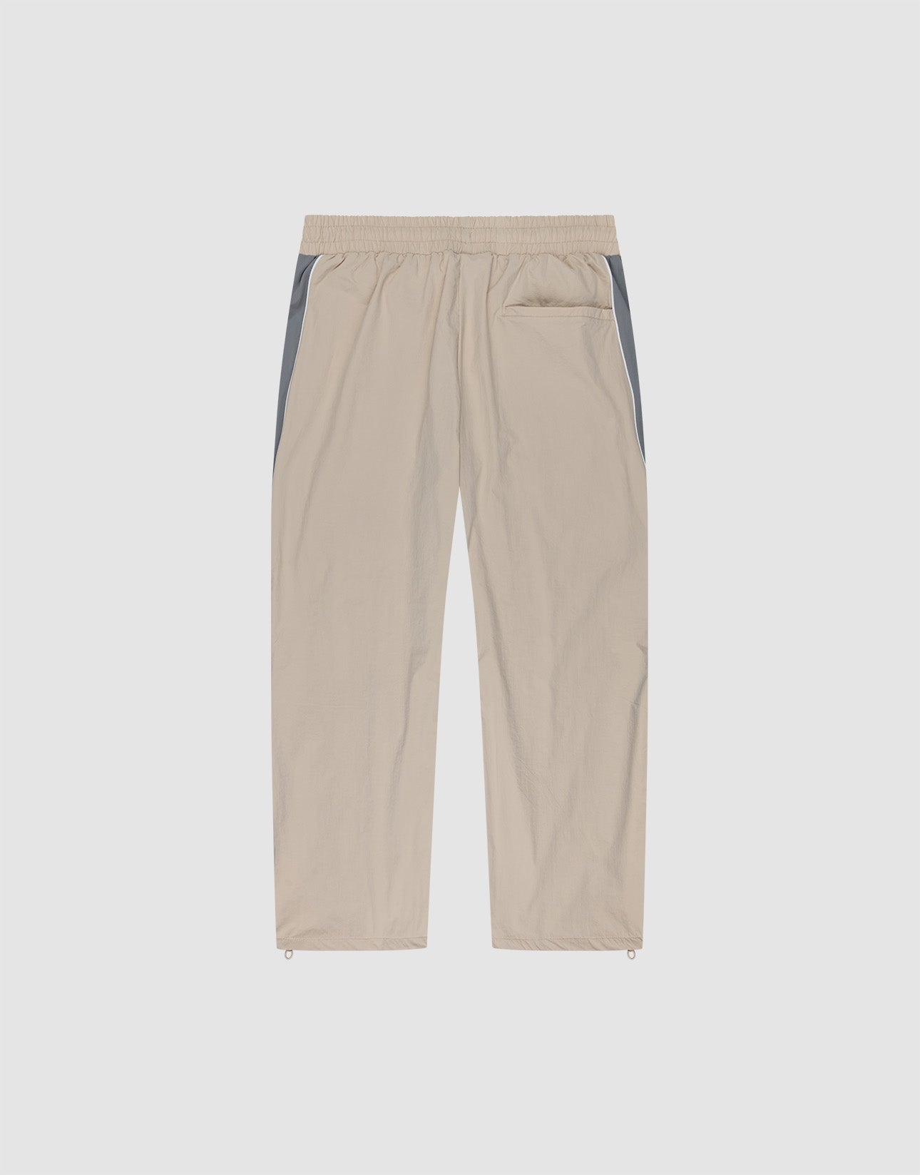 The LIVE FAST DIE YOUNG Basic Nylon Trackpants feature a wide fit, elastic waistband, straight beige legs with grey side panels, single back pocket, and adjustable ankle drawstrings—shown against a plain white background.