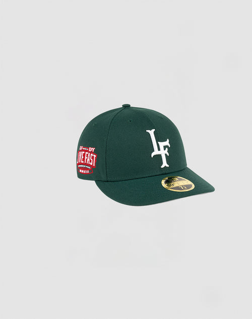 The LFDY x NEW ERA 59FIFTY Low Profile by LIVE FAST DIE YOUNG is a dark green fitted cap with a white LF logo front, red LIVE FAST side patch, and gold brim sticker, displayed on a plain light gray background.