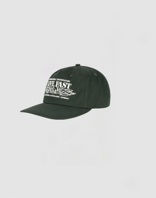 The LIVE FAST DIE YOUNG Live Fast Corporation Cap is a dark green 5-panel cap with a curved brim and snapverschluss, featuring bold white multi-logo graphic text on the front panel, shown against a plain light gray background.