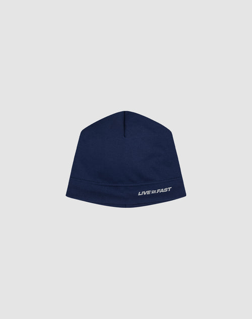 The Live Fast Performance Beanie by LIVE FAST DIE YOUNG is a navy blue, polyester fitted beanie with a reflective LIVE FAST logo in small white letters on the lower edge, shown against a plain light gray background.