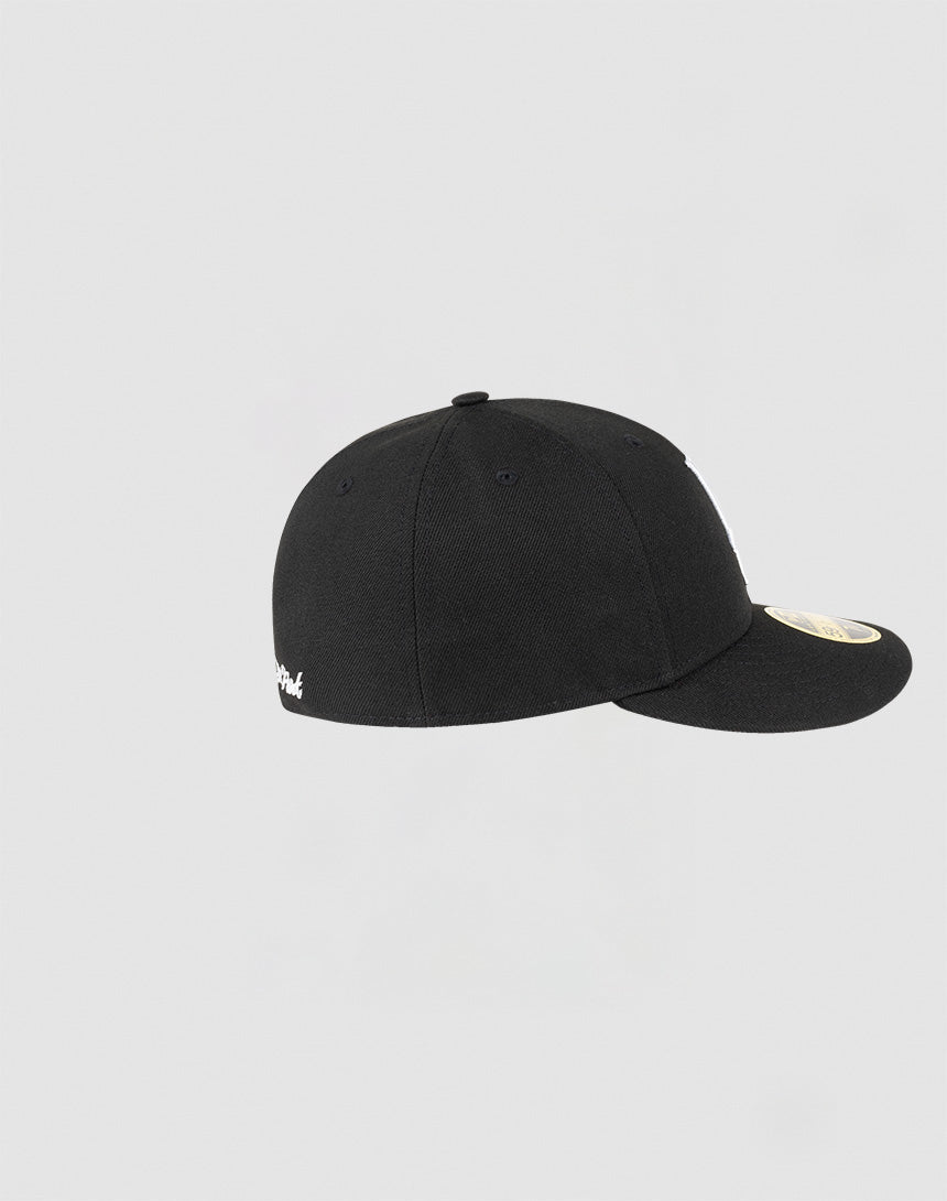 The LFDY x NEW ERA 59FIFTY Low Profile cap by LIVE FAST DIE YOUNG is shown from the side on a plain light gray background, highlighting its low profile shape, flat brim, and white circular sticker on the visor.