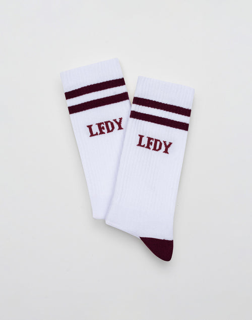 The LIVE FAST DIE YOUNG 2 Tone Socks (2 Pack) are white crew socks with two maroon stripes, LFDY embroidery, and maroon toes and heels. Made from pflegeleicht Baumwolle and Polyamid. Displayed on a plain white background.