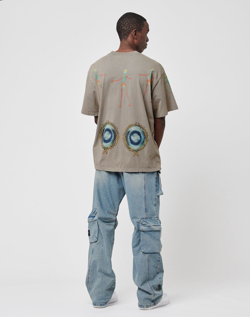 A person stands facing away, wearing the LIVE FAST DIE YOUNG Died for It Tee in gray with abstract colorful back graphics, light blue cargo jeans with a vintage effect, and white sneakers against a plain white background.