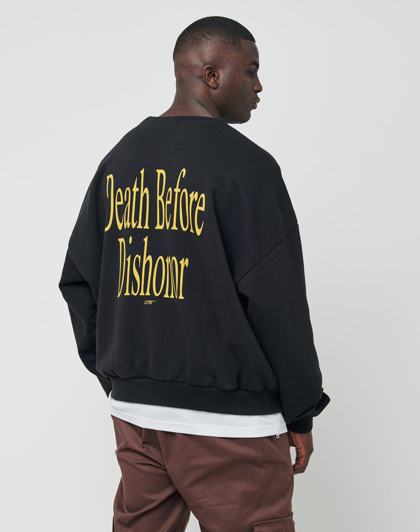 A person in the LFDY Death Before Dishonor Sweater, featuring bold yellow Death Before Dishonor text on the back, stands sideways against a plain light background.