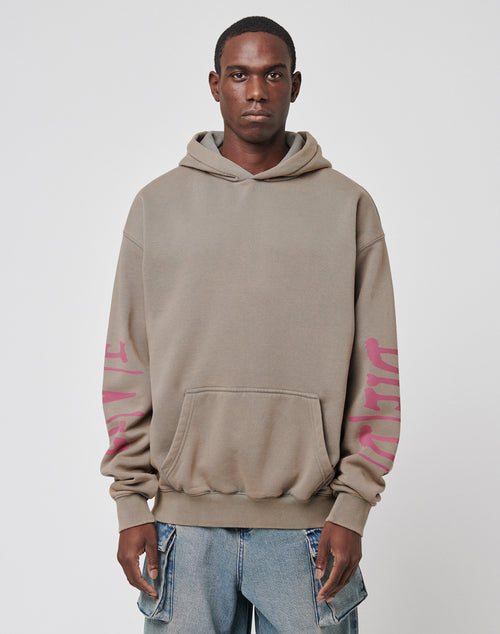 A person wears the LIVE FAST DIE YOUNG Godfathers Hooded, a loose taupe hoodie with pink sleeve writing and blue jeans, standing against a white background. Its oversize fit and Vintage Effekt give it effortless style.