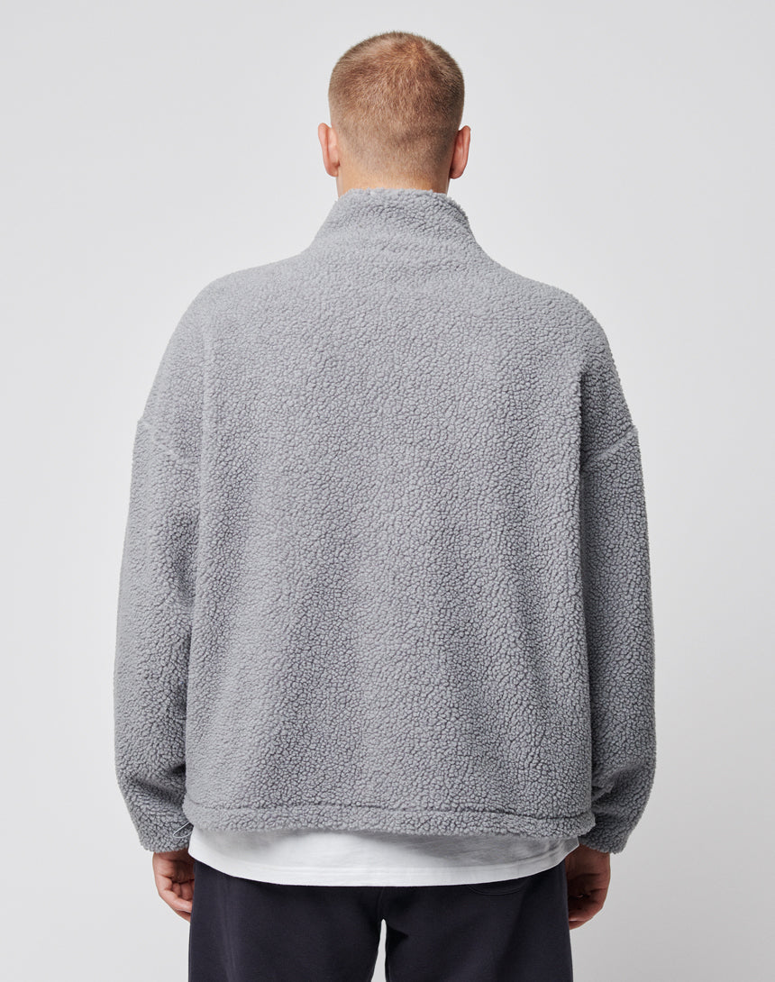 A person with short hair is seen from behind wearing the LIVE FAST DIE YOUNG Oversize Teddy Jacket in light gray fleece over a white shirt and dark pants, standing against a plain light background.