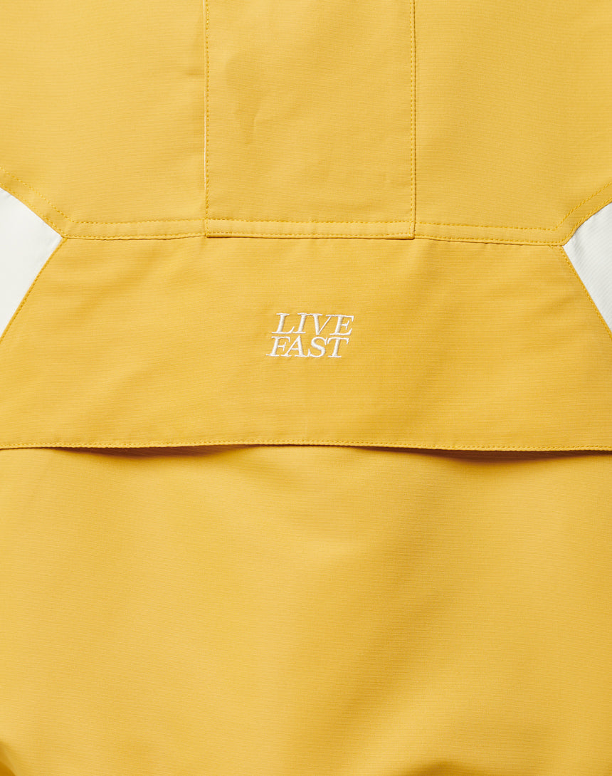 Close-up of the Half Zip Hooded Jacket by LIVE FAST DIE YOUNG, featuring yellow fabric with white stitched LIVE FAST text and sporty white diagonal stripes on both sides.