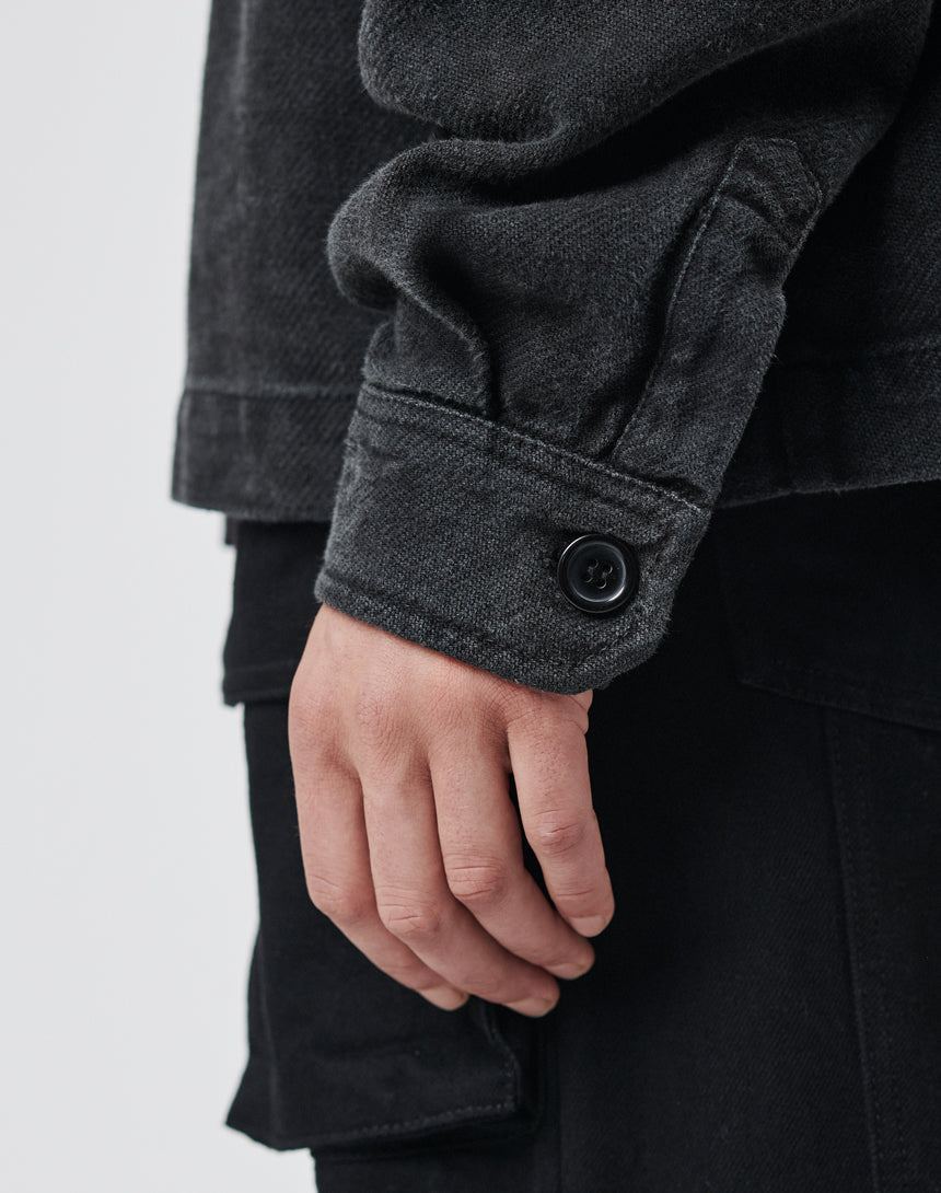 A close-up of a person’s hand by their side, wearing the LIVE FAST DIE YOUNG Vintage Dyed Flannel in an oversize fit and black pants with a pocket flap, set against a plain, light-colored background.