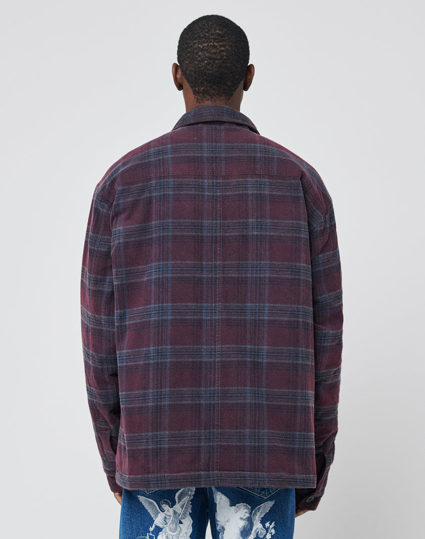 A person facing away from the camera wears a LIVE FAST DIE YOUNG Padded Flannel Jacket in burgundy and navy plaid with a vintage effect and blue jeans featuring white graphic designs, standing against a plain light background.