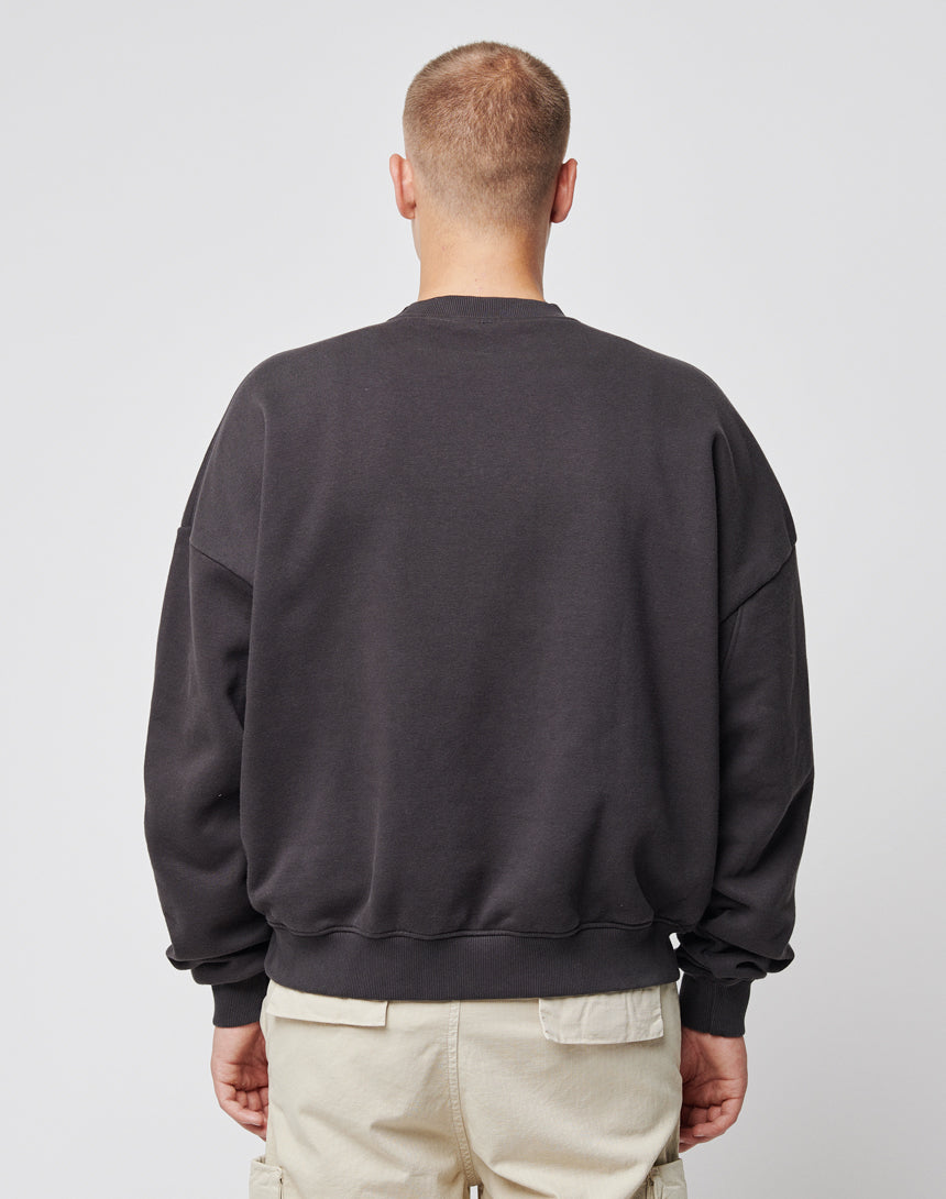 A person with a buzzcut stands facing away from the camera, wearing the LIVE FAST DIE YOUNG Live Fast Die Young Chest Sweater and light-colored cargo pants against a plain white background.