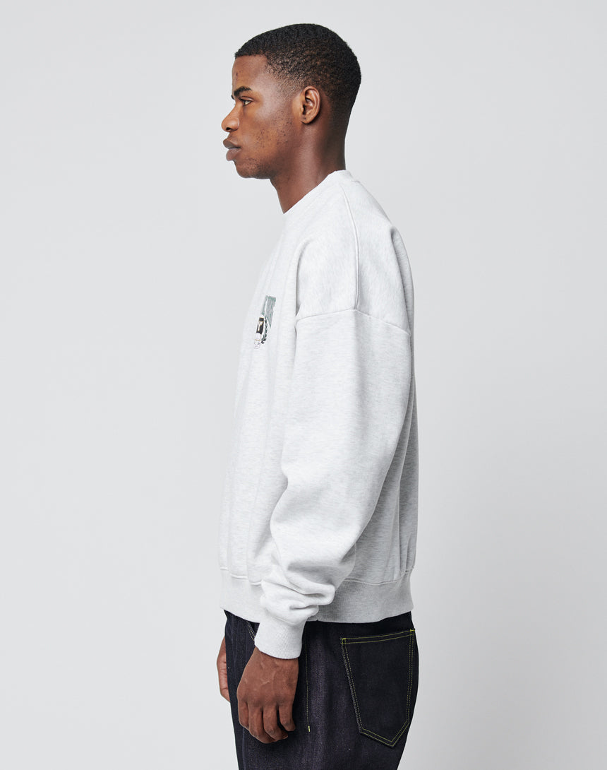 A man in profile faces left, wearing the LIVE FAST DIE YOUNG Live Fast Die Young Chest Sweater—an oversize fit in light gray with a subtle vintage effect—and dark jeans, set against a plain light gray background.