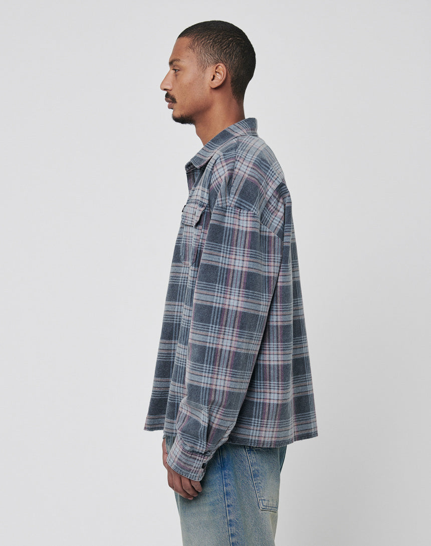 A man with short hair wears the LIVE FAST DIE YOUNG Loose Flannel Shirt in blue and gray plaid, made from 100% Baumwolle, styled with light blue jeans and standing in profile against a plain, light background.