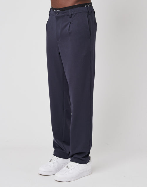 A person models LIVE FAST DIE YOUNG Regular Casual Pants in dark navy blue with an elastic waistband and white sneakers, standing against a plain white background. Only the lower body is shown.