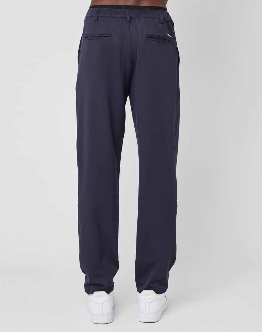 A person faces away, wearing navy blue LIVE FAST DIE YOUNG Regular Casual Pants with an elastic waistband and rear welt pockets, paired with white sneakers, set against a plain white background.