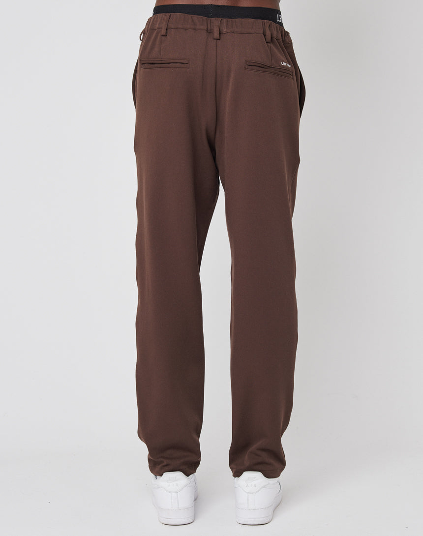 A person faces away in LIVE FAST DIE YOUNG Regular Casual Pants with an elastic waistband and back zipper pockets, paired with white sneakers, set against a plain light background.