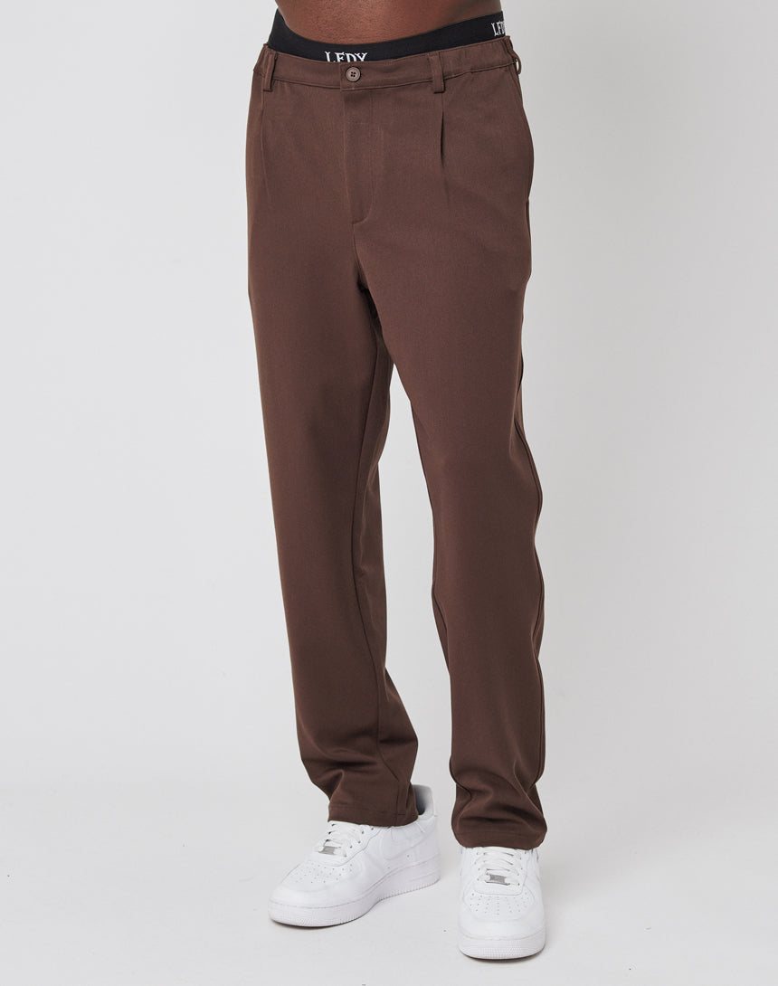 A person in LIVE FAST DIE YOUNG Regular Casual Pants with elastischer Bund, white sneakers, and black LFNY waistband underwear stands against a plain white background.