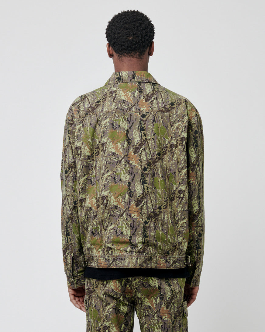 A person stands facing away from the camera, wearing a LIVE FAST DIE YOUNG LFDY Hunter Jacket and matching 100% Baumwolle pants in a green and brown camouflage pattern, set against a plain light background.