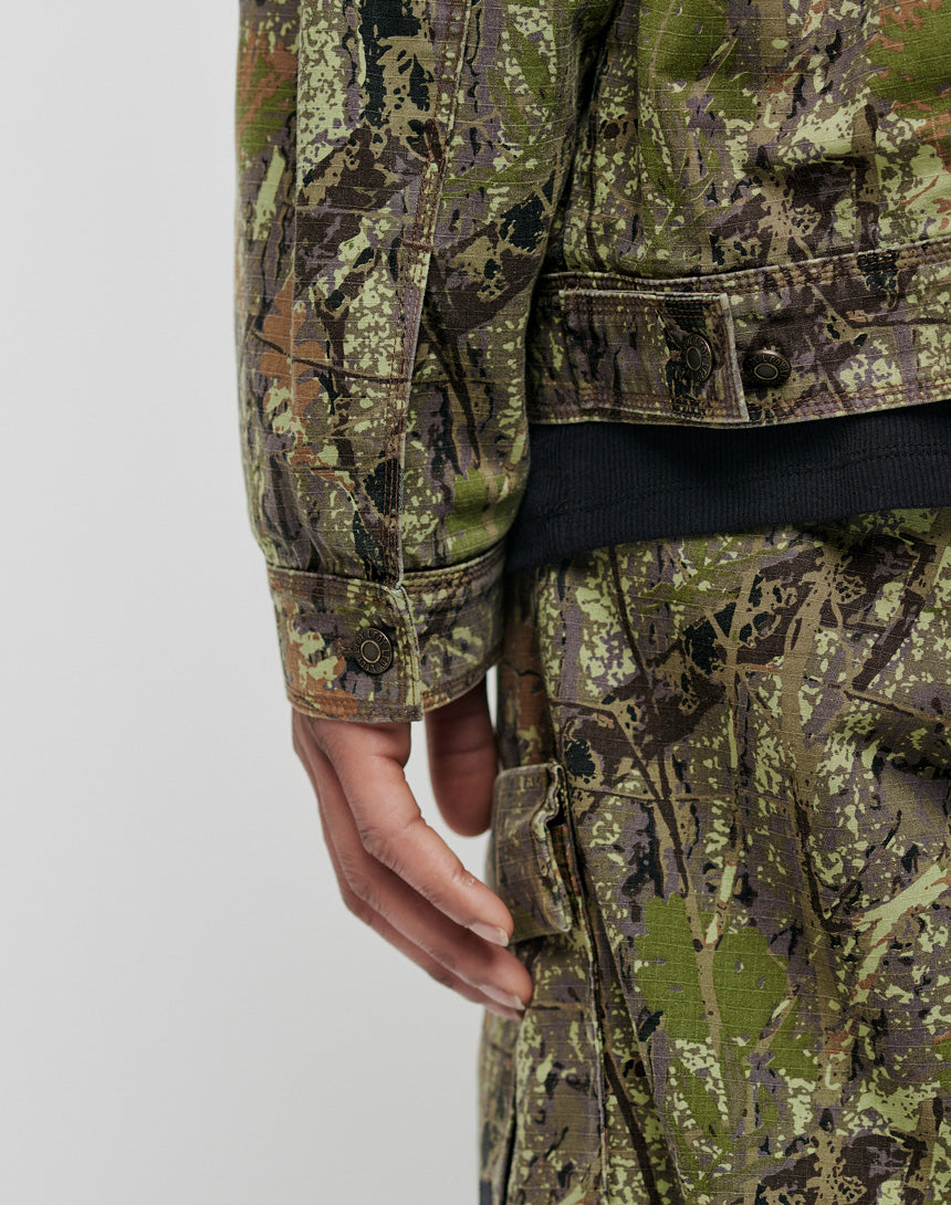 A close-up of a person wearing the LFDY Hunter Jacket by LIVE FAST DIE YOUNG, made from 100% Baumwolle, shows their hand resting near their leg against a plain light background.
