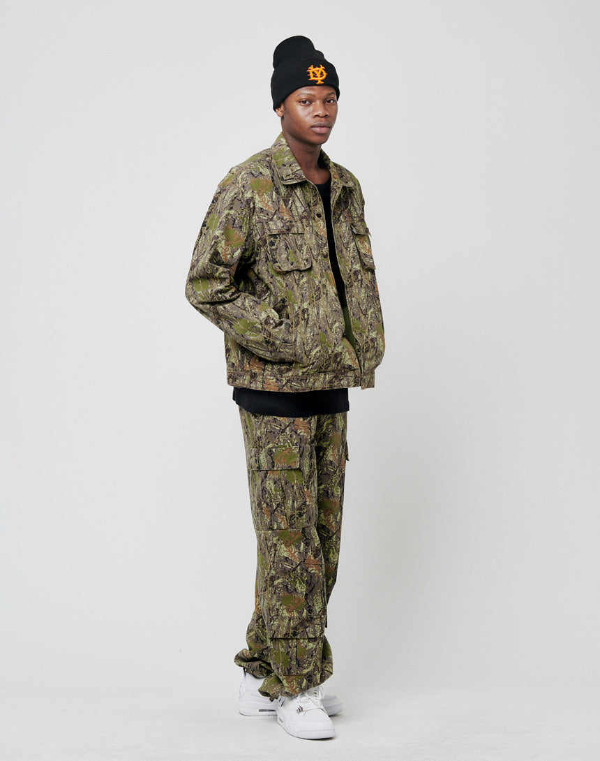 A person stands against a plain background wearing the LIVE FAST DIE YOUNG LFDY Hunter Jacket and matching pants made from 100% Baumwolle, styled with a black T-shirt, a black beanie with orange lettering, and white sneakers.