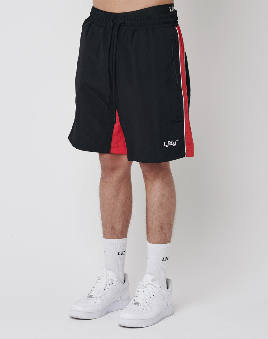 A person wears LFDY Beach Shorts in black with red and white side panels, white LF socks, and white sneakers against a white backdrop. The shorts have an elastic waistband, Lfdy on the left hem, and a comfortable mesh inlay.