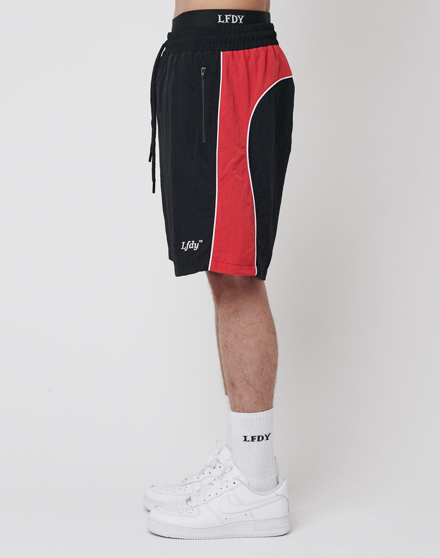A person stands sideways wearing black and red LFDY Beach Shorts, white LFDY crew socks, and white sneakers against a plain white background.