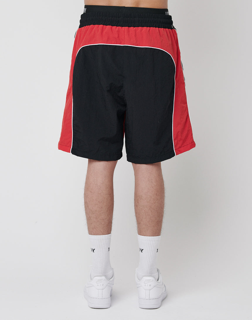 A person faces away, wearing LFDY Beach Shorts in black and red with mesh inlay and white trim, paired with white socks and sneakers, set against a plain background.