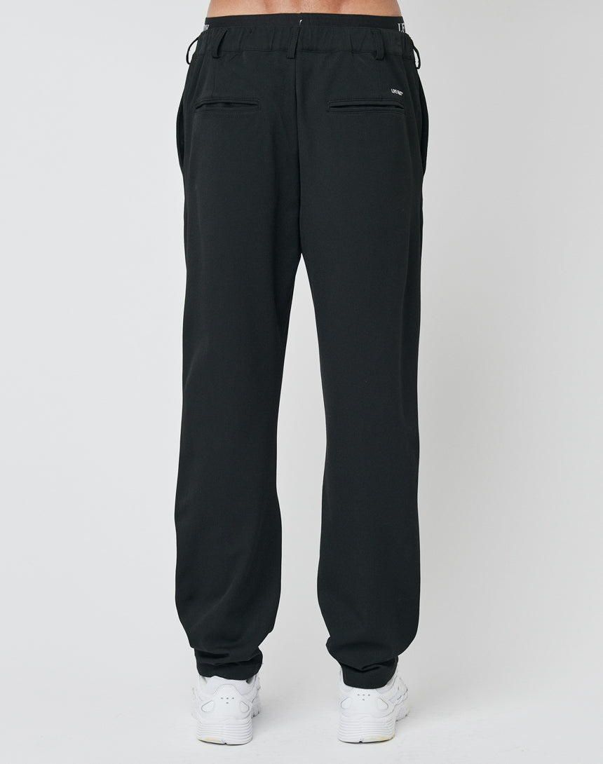 A person is seen from the back, waist down, wearing LFDY Regular Casual Pants in black with an elastic waistband and back pockets, styled with white sneakers against a plain white background.
