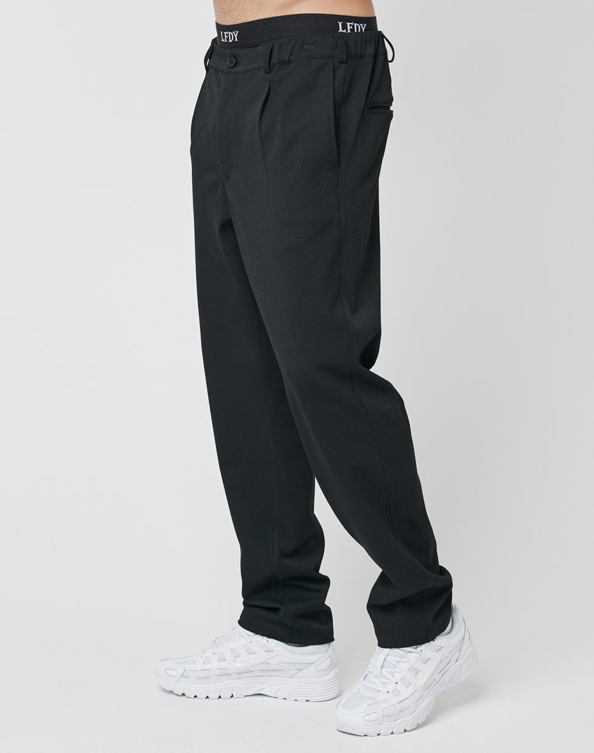 A person wears black Regular Casual Pants from LFDY with an elastic waistband featuring LFDY, paired with white athletic sneakers, standing against a plain white background.