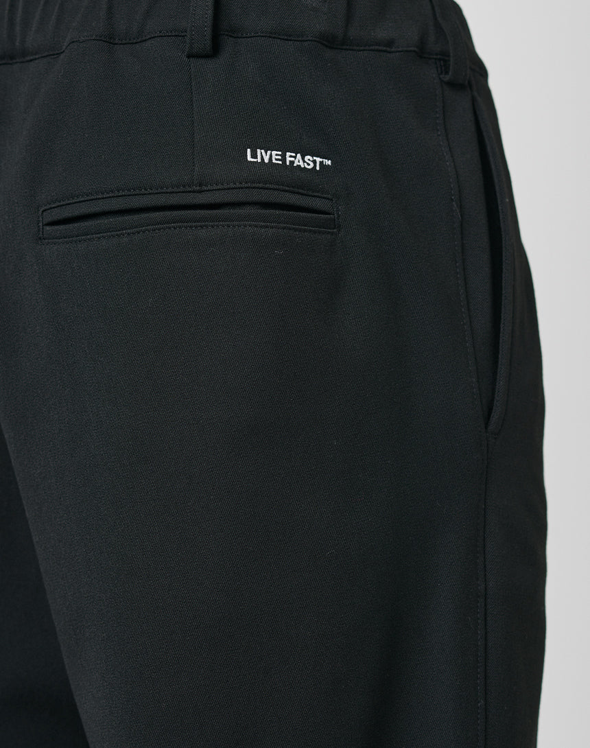Close-up of LFDY Regular Casual Pants in black with a regular fit, elastic waistband, back and side pockets, and LIVE FAST⢠white text above the back pocket.