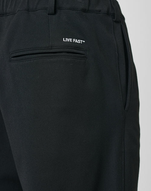 Close-up of LFDY Regular Casual Pants in black with a regular fit, elastic waistband, back and side pockets, and LIVE FAST™ white text above the back pocket.
