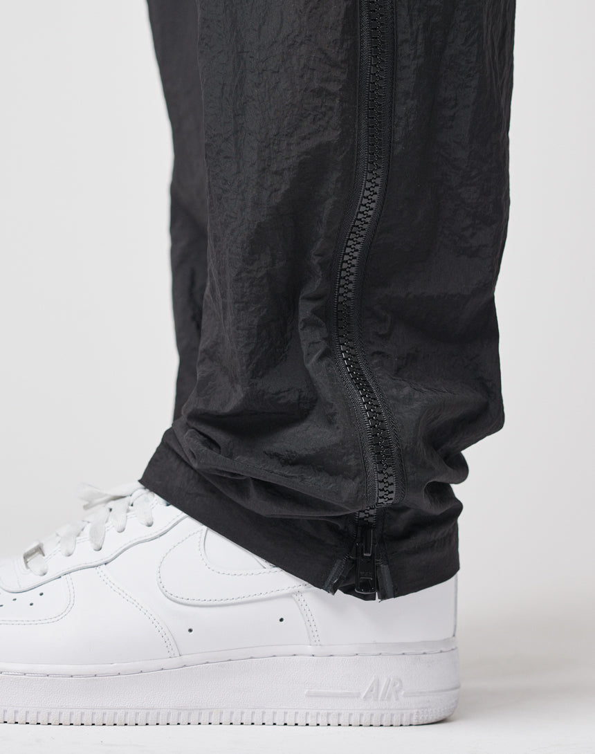 Close-up of a person wearing white Nike Air Force 1 sneakers and black LFDY Zip Tape Track Pants, featuring a vertical ankle zipper.