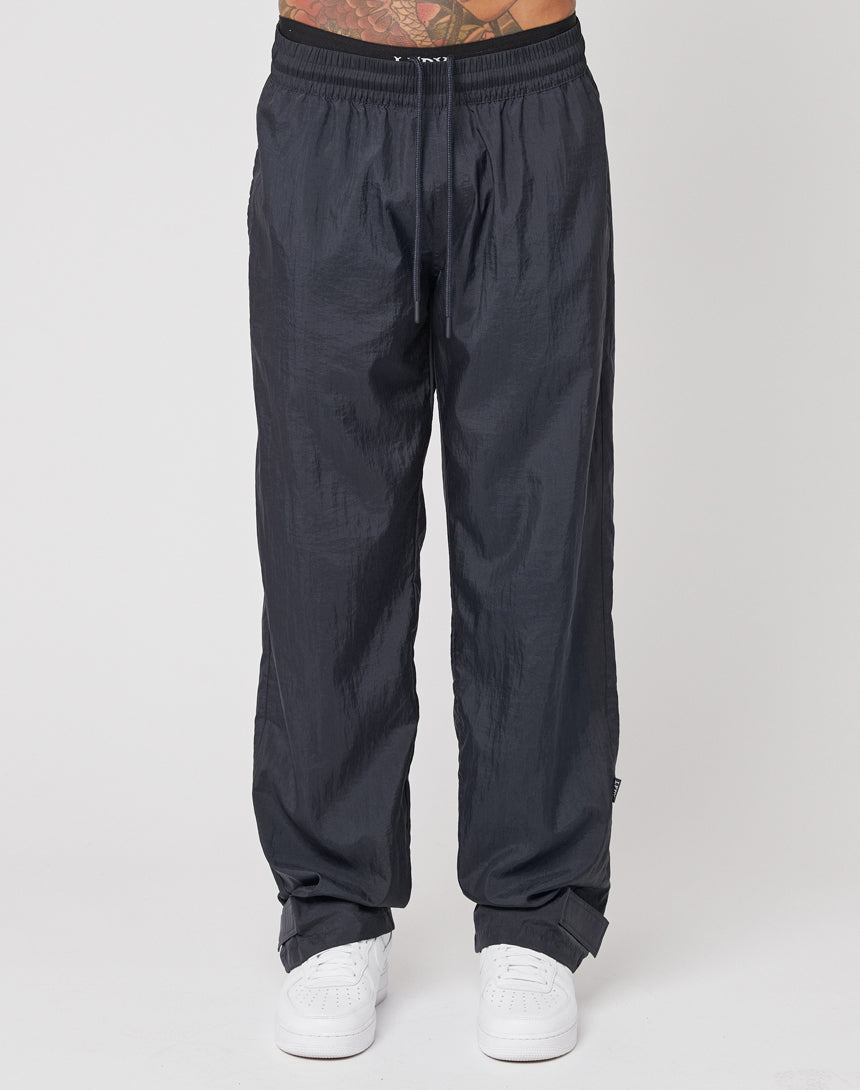 A person wearing LIVE FAST DIE YOUNG Nylon Jogger track pants in regular fit with an elastic waistband and white sneakers stands against a plain white background. Only the lower body is visible.