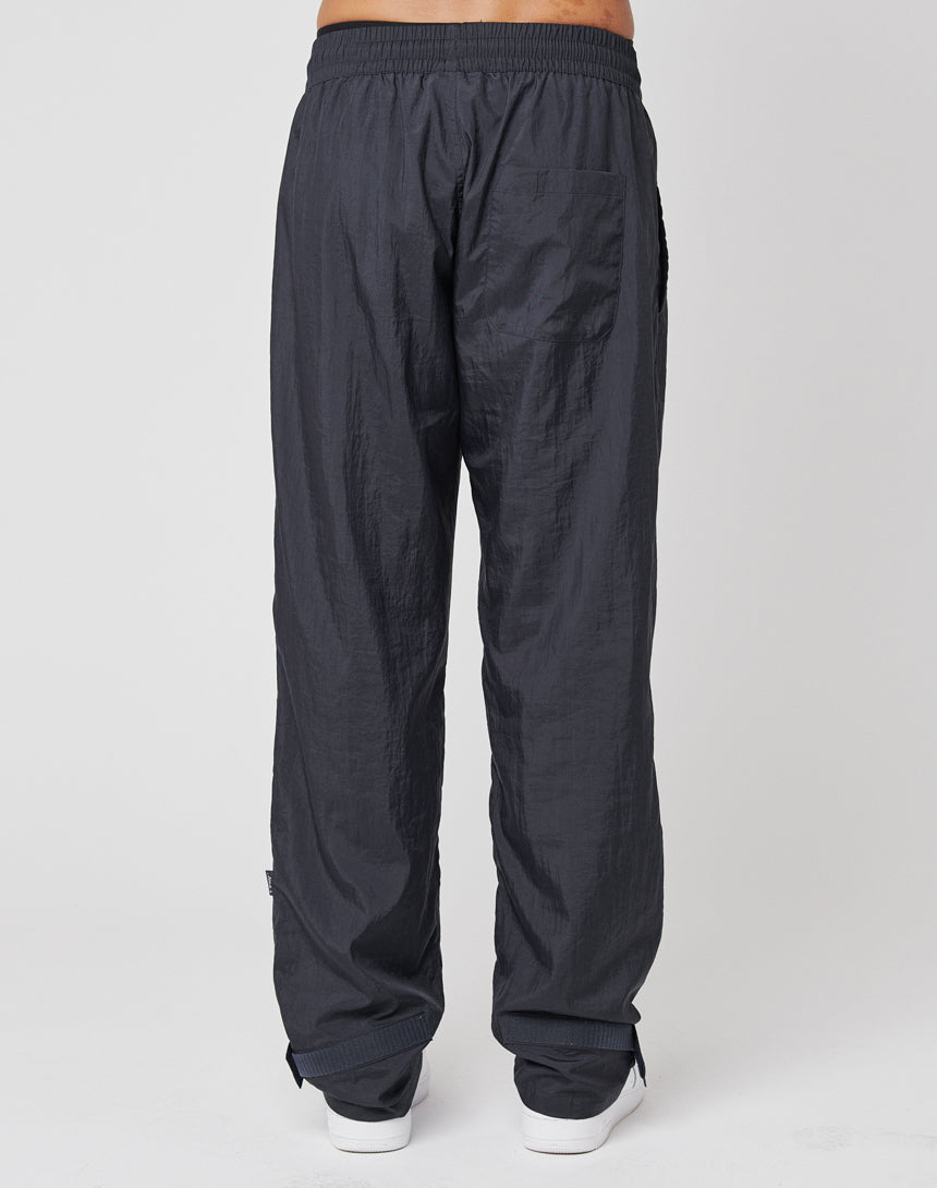 A person models the LIVE FAST DIE YOUNG Nylon Jogger, featuring a breiter Elastikbund and cuffs in loose-fitting, dark gray nylon. Only the lower half is visible against a plain light background.