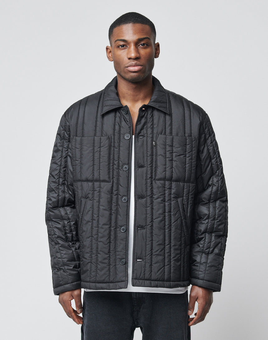 A man faces forward wearing a LIVE FAST DIE YOUNG Import & Export Jacket over a gray shirt and black jeans, set against a plain light gray background.
