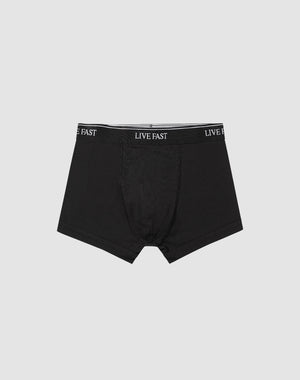A pair of black Live Fast Trunks (2 Pack) by LIVE FAST DIE YOUNG, made from soft cotton with LIVE FAST repeatedly printed in white on the elastic waistband, displayed on a plain light gray background.